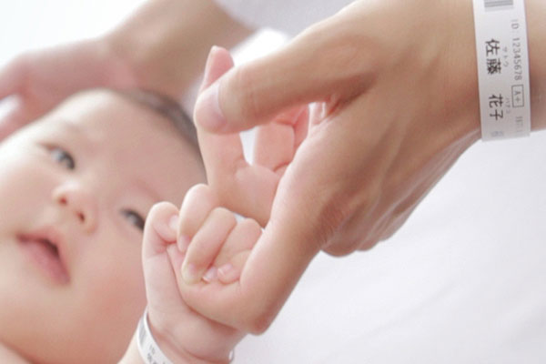 Baby in hospital holding parent&rsquo;s finger - both are wearing wristbands